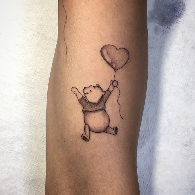 Simple tattoo of Winnie the Pooh floating with a heart-shaped balloon on a person's forearm